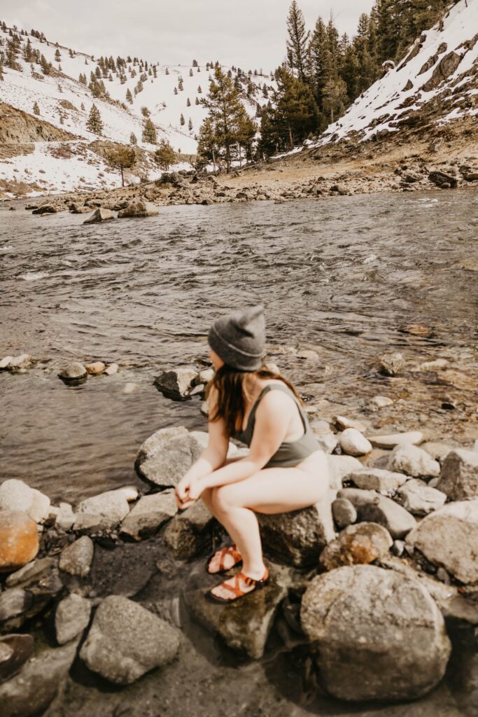 Woman in beanie and swimsuit sitting in a natural hot spring in Idaho.