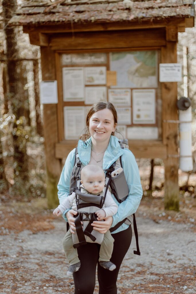 Woman with baby in baby carrier standing in front of King Creek Falls trailhead sign.