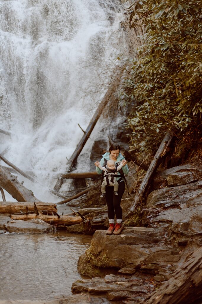 Woman with baby in baby carrier standing in front of King Creek Falls in South Carolina.