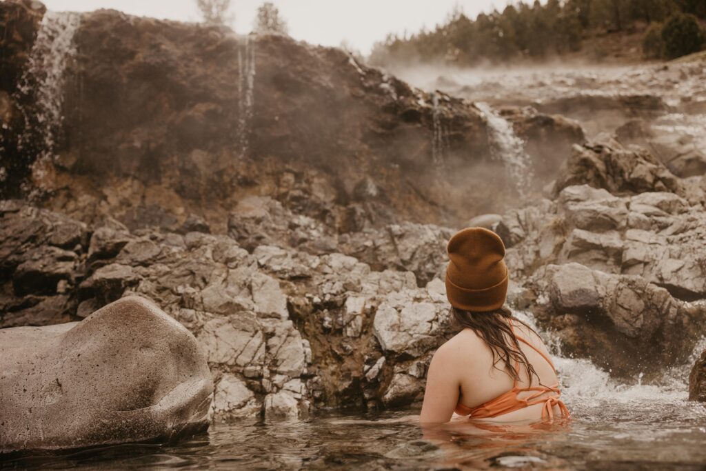 Woman in beanie and swimsuit sitting in a natural hot spring in Idaho.