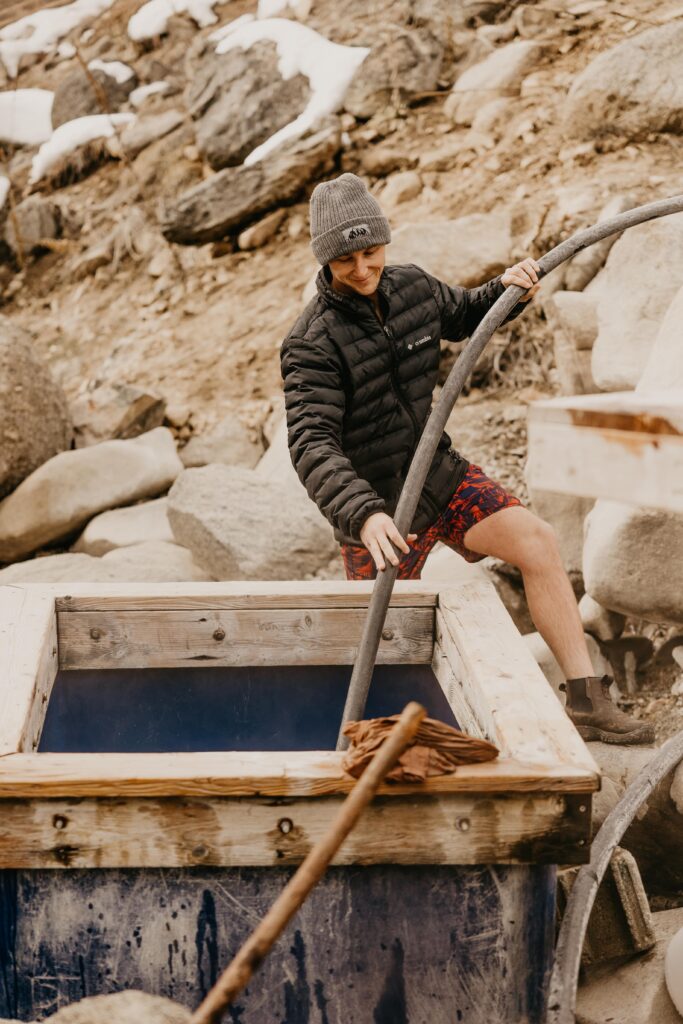 Man in beanie and jacket filling up a natural hot spring box in Idaho.