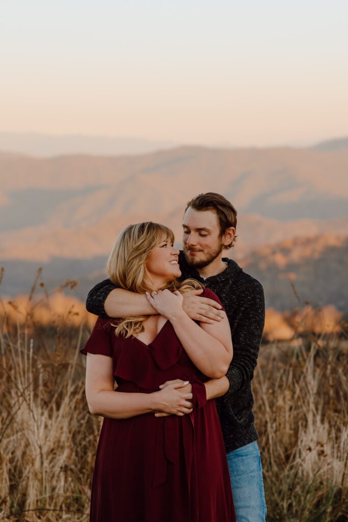 Man hugging and kissing woman from behind during sunset photoshoot at Max Patch Mountain in North Carolina.