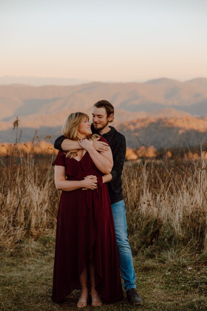 Man hugging woman from behind during sunset photoshoot at Max Patch Mountain in North Carolina.