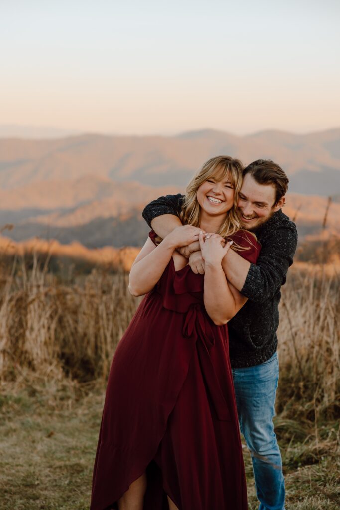 Man hugging woman from behind during sunset photoshoot at Max Patch Mountain in North Carolina.