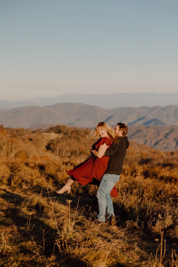 Man picking woman up and spinning during sunset photoshoot at Max Patch Mountain in North Carolina.