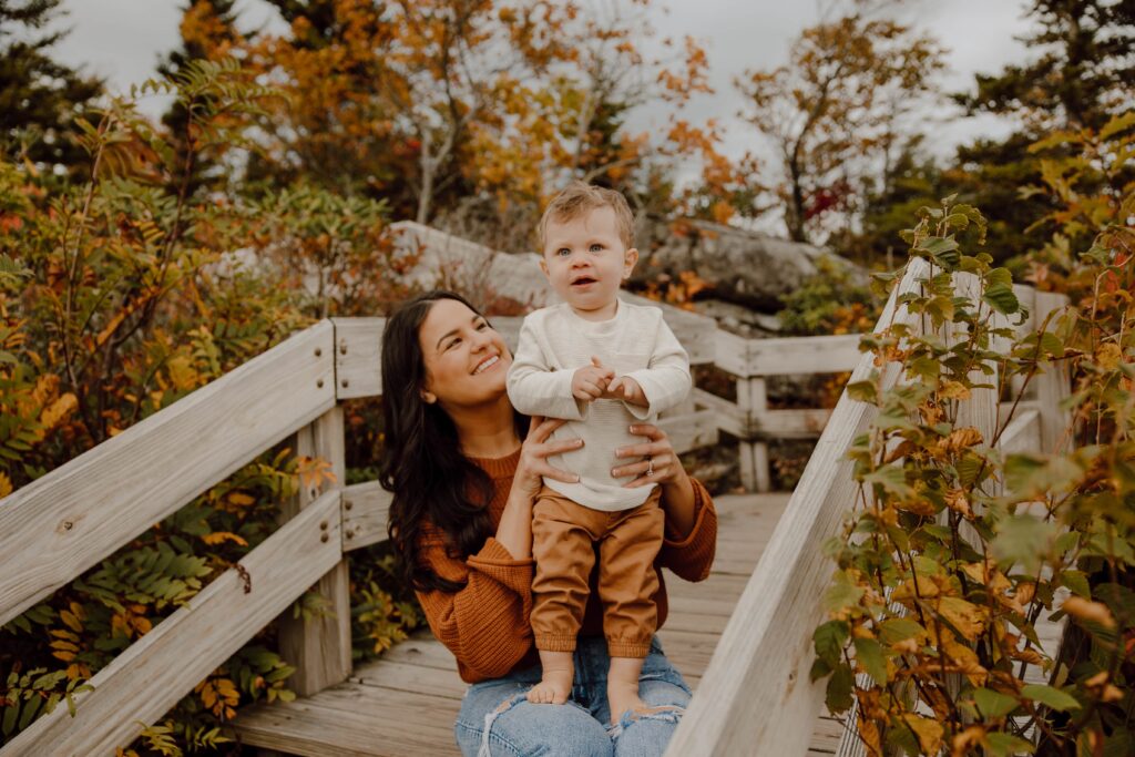 Woman holding baby during fall photoshoot at Rough Ridge overlook in Boone, NC.