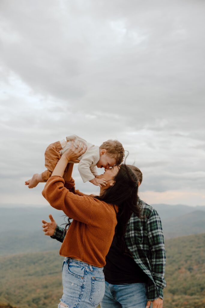 Woman holding baby up in the air with foreheads touching during fall photoshoot at Rough Ridge overlook in Boone, NC.