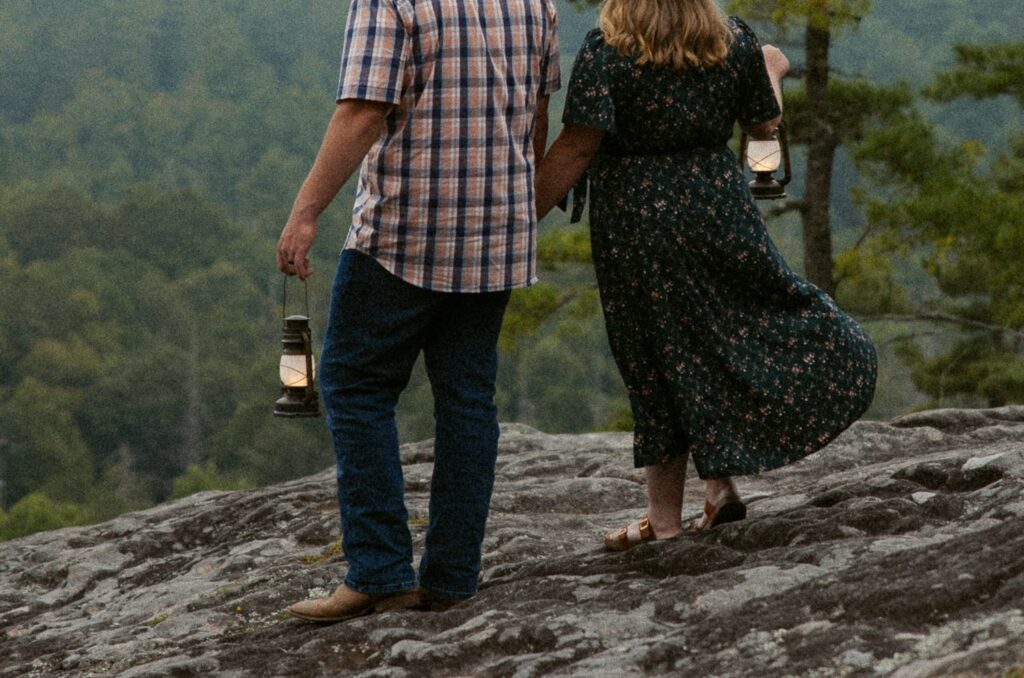 Man and woman standing on rock and holding lanterns during engagement photos.
