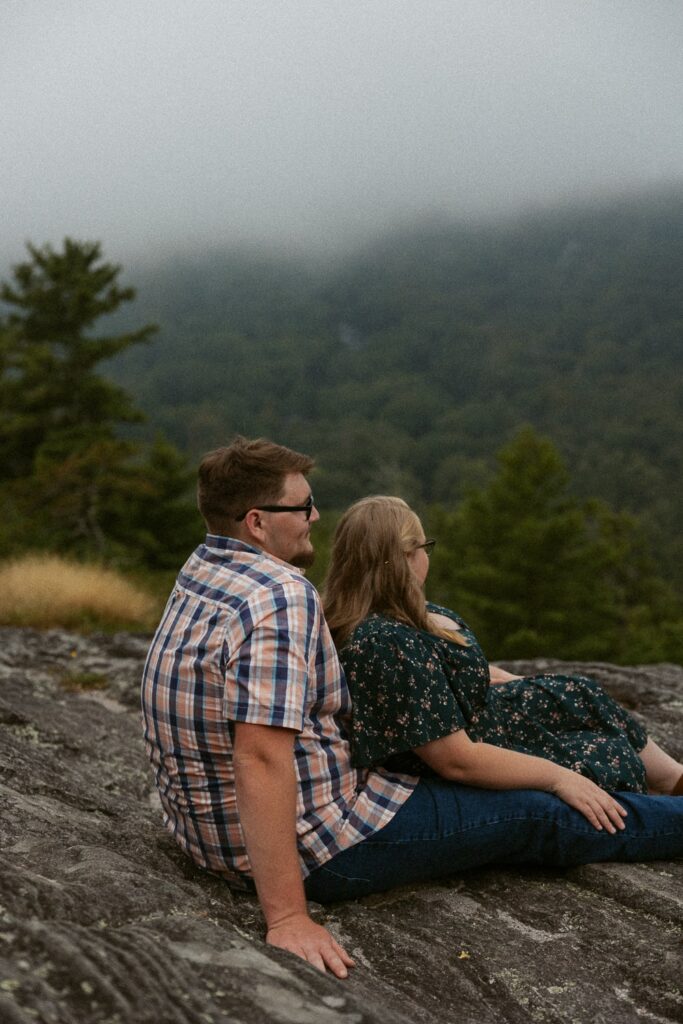 Man and woman sitting on rock and looking at the foggy mountains.