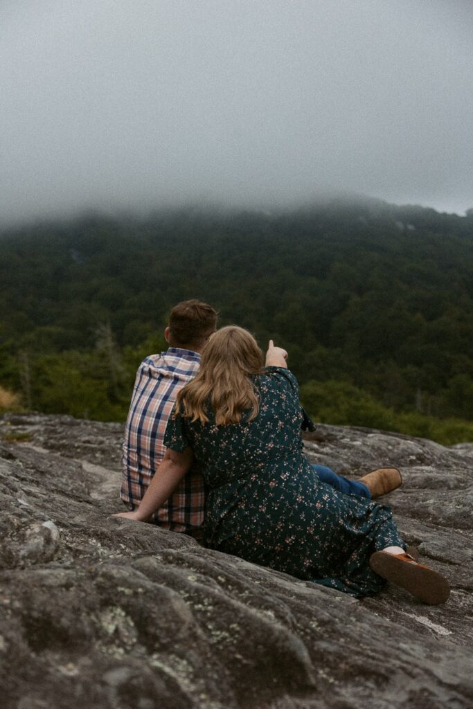 Man and woman sitting on rock and looking at foggy mountains.