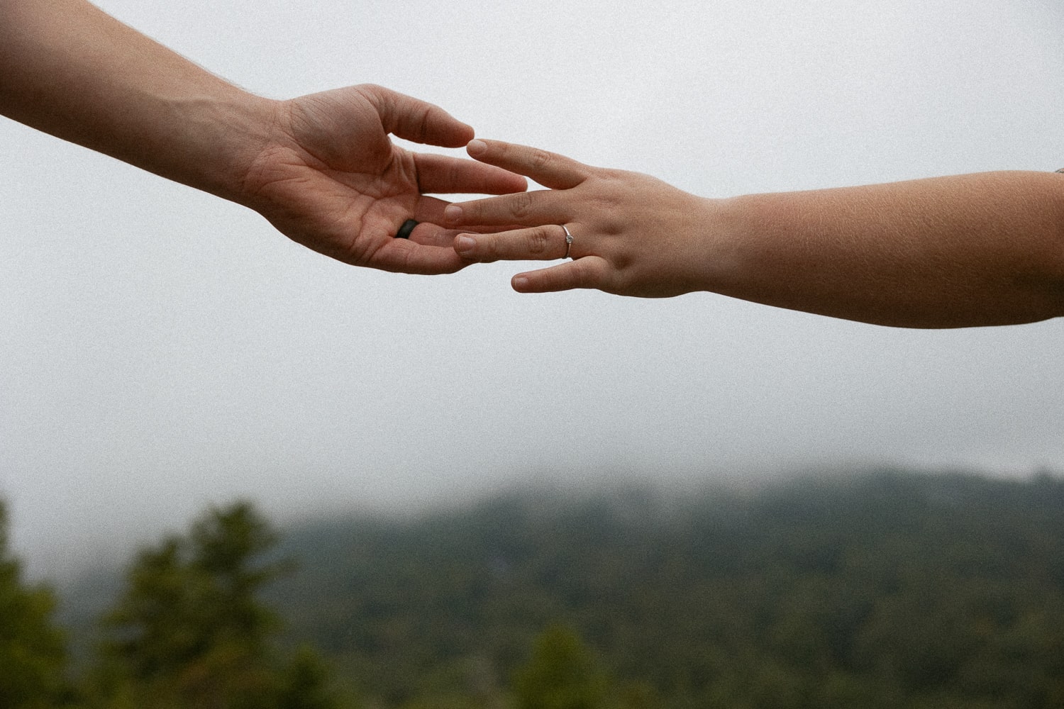Man and woman hands touching with mountains in the background.