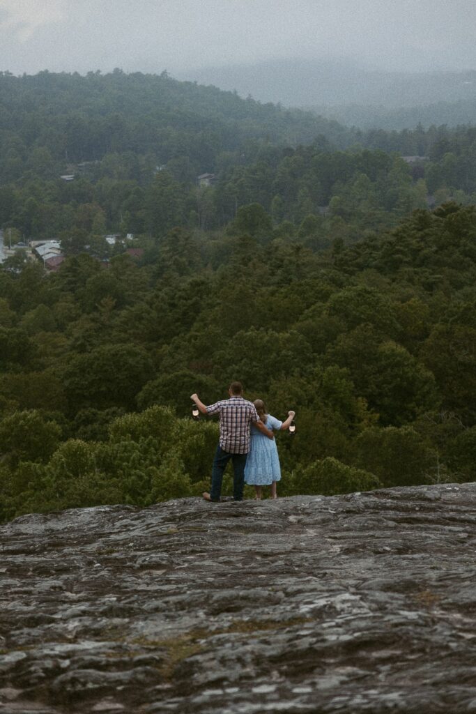 Man and woman standing on rock looking at mountains while holding lanterns.