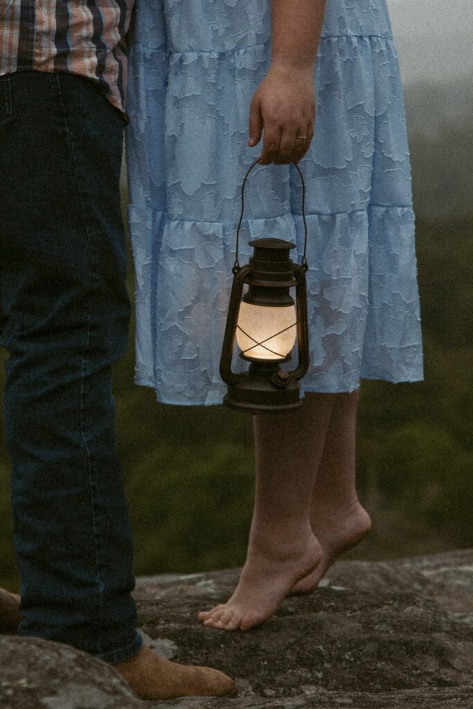 Woman standing on tippy toes and holding lantern during engagement photos.