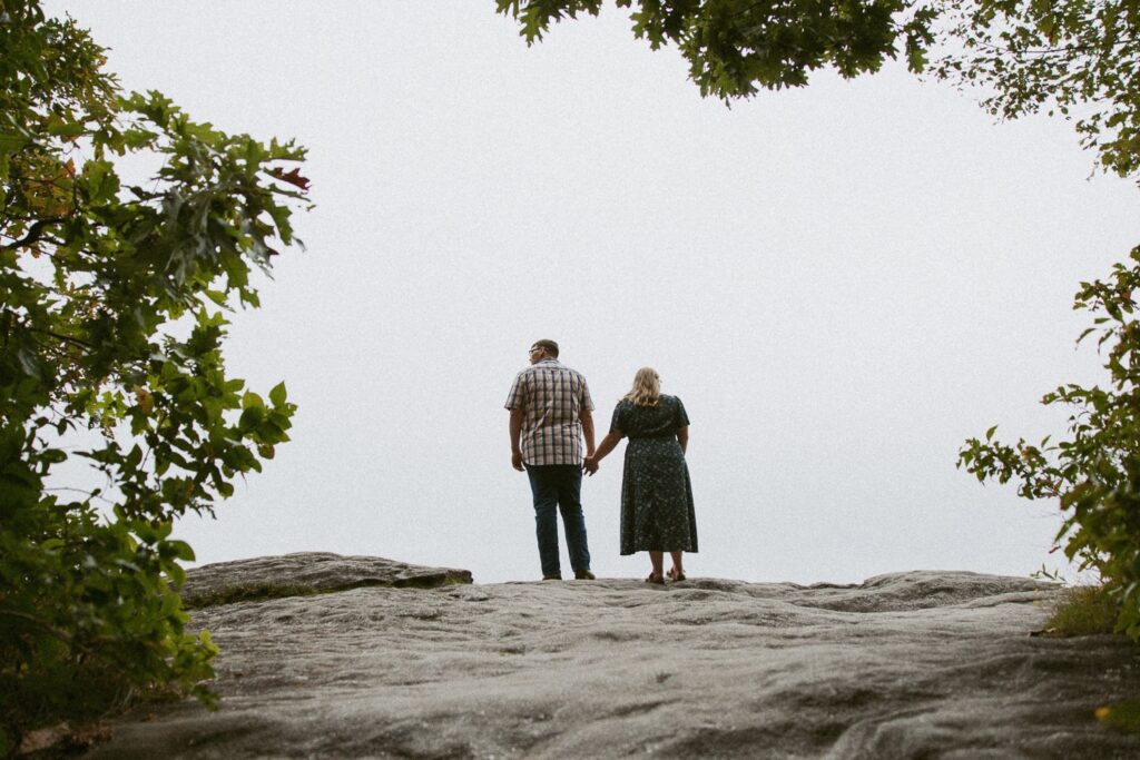 Man and woman standing on rock and holding hands at Sunset Rock in Highlands, North Carolina.