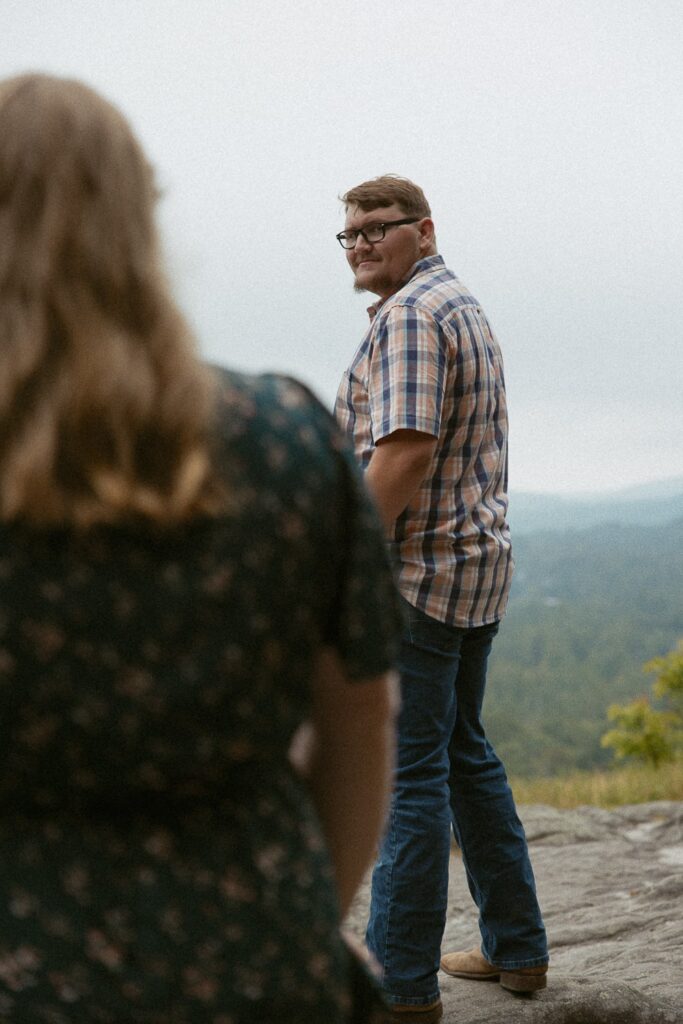 Man looking at woman during engagement photos at Sunset Rock in Highlands, North Carolina.