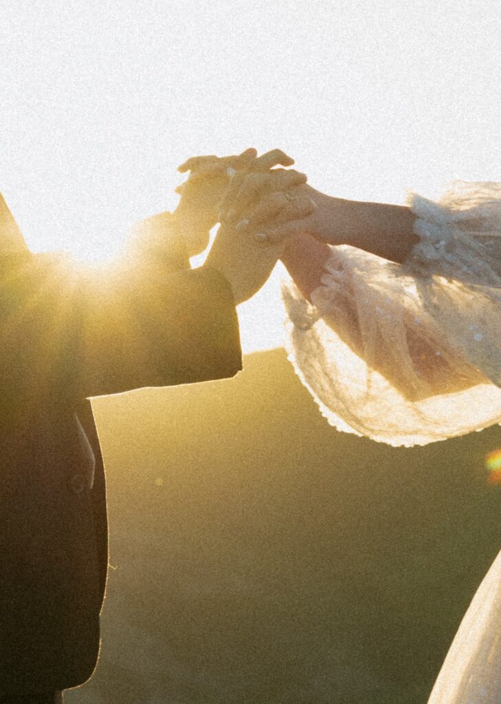 Close up of man and woman holding hands with sun shining behind them.
