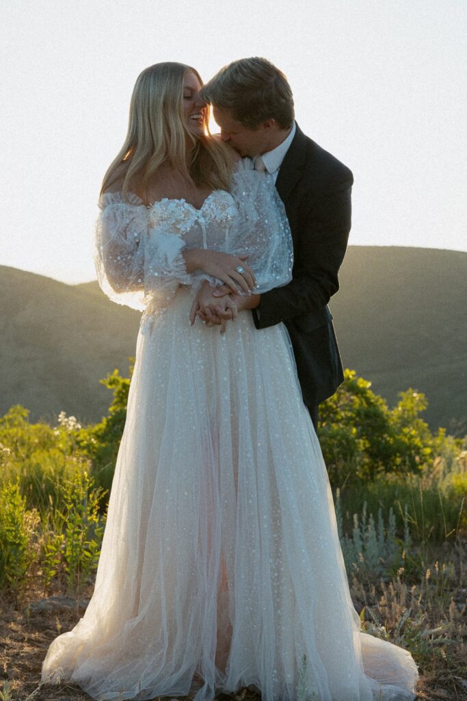 Man and woman in wedding attire and hugging each other with mountains in the background.
