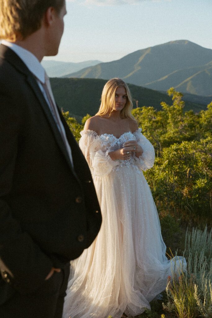 Woman in wedding dress looking at man in suit with mountains in the background.