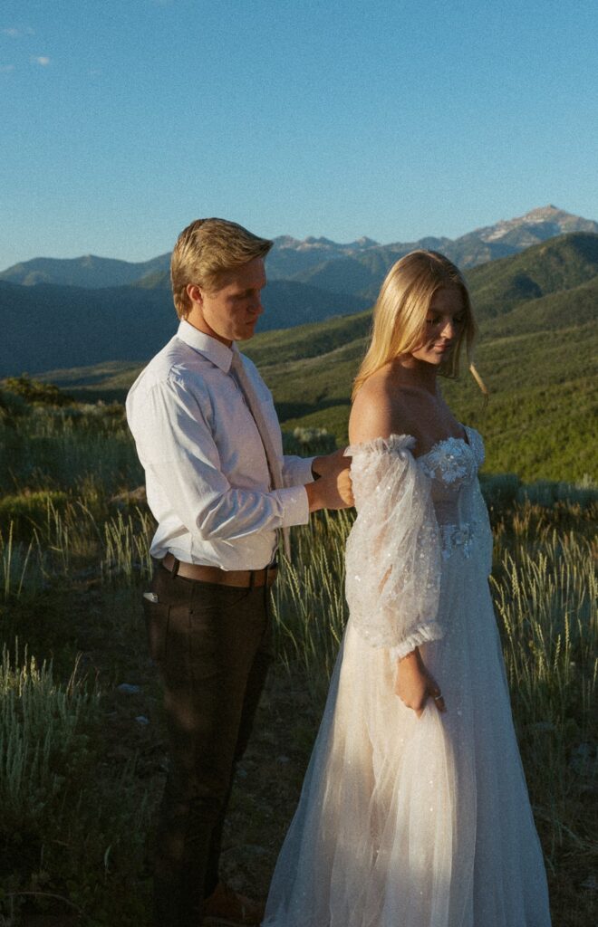 Man zipping up woman's wedding dress during elopement in the mountains.