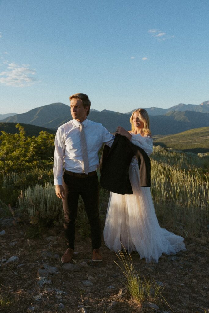 Woman helping man put on his suit jacket during elopement in the mountains.