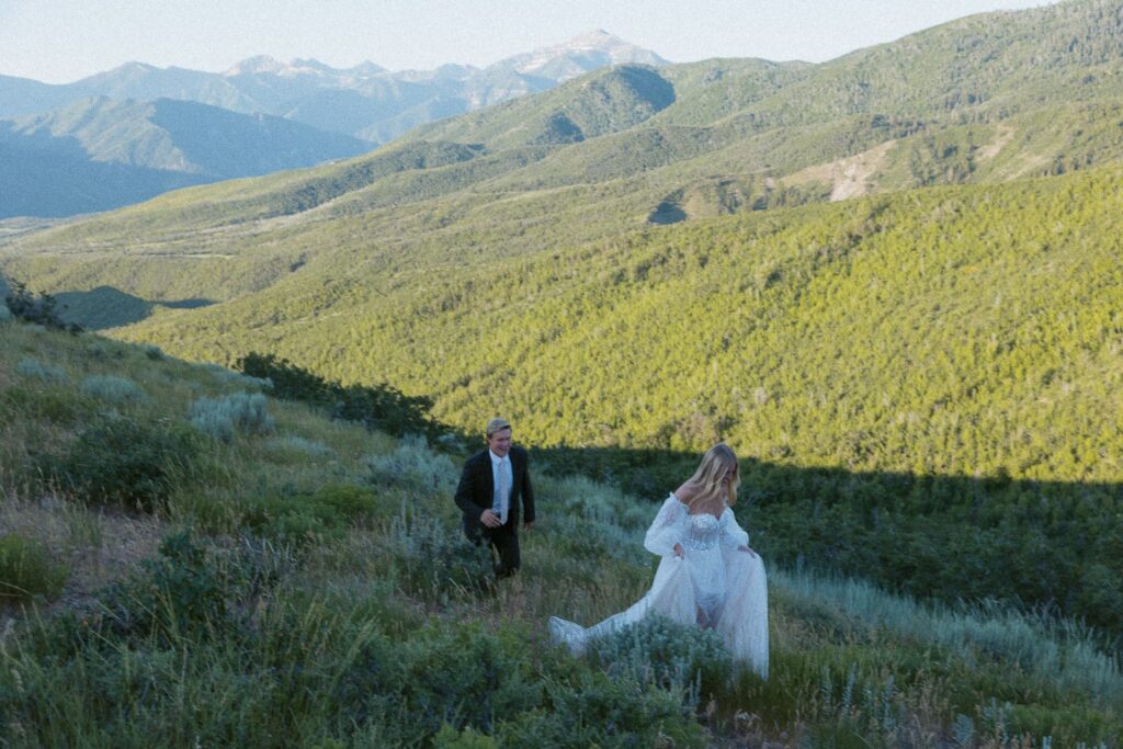 Man chasing a woman through a field during elopement with mountains in the background.