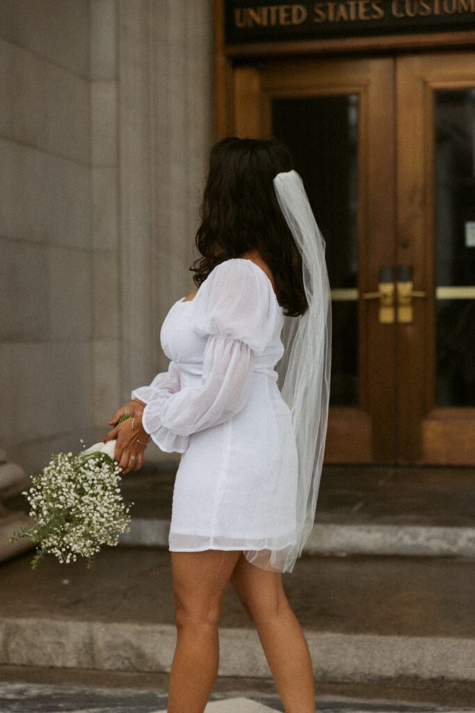 Woman in wedding dress and holding flowers in front of courthouse. 