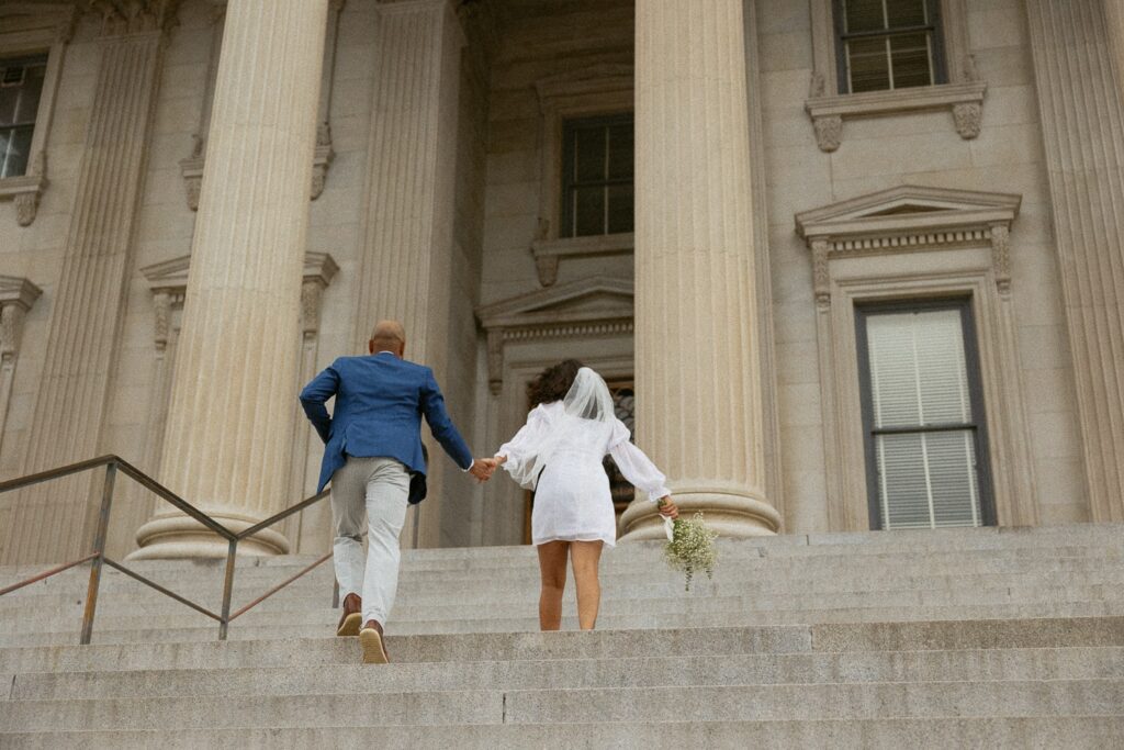 Man and woman running up courthouse steps in Charleston in wedding attire. 