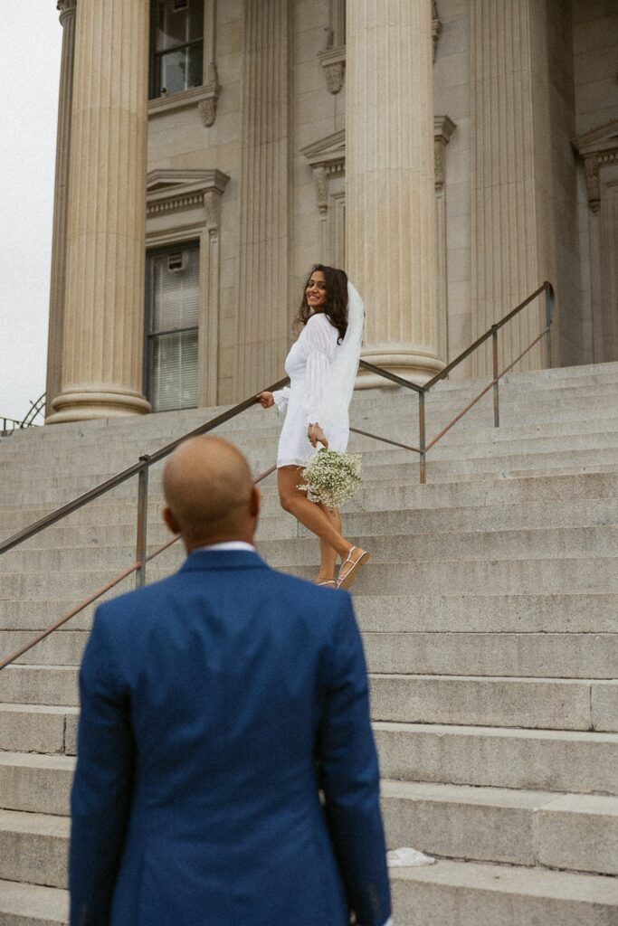 Man looking at woman standing on courthouse steps in wedding attire.