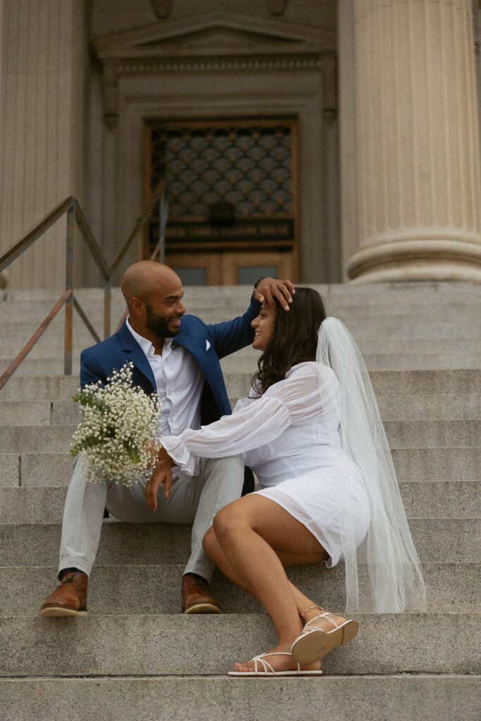 Man brushing woman's hair out of her face while sitting on courthouse steps in Charleston in wedding attire.