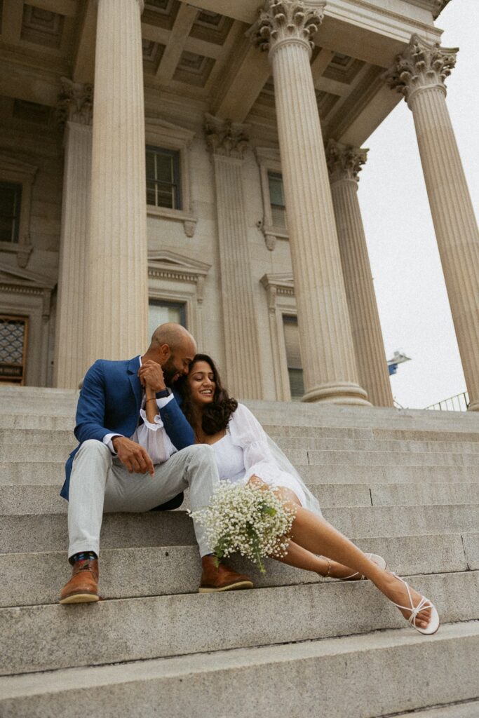Man and woman dressed in wedding attire and sitting on courthouse steps.