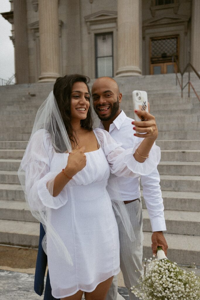 Man and woman taking a selfie while dressed in wedding attire. 