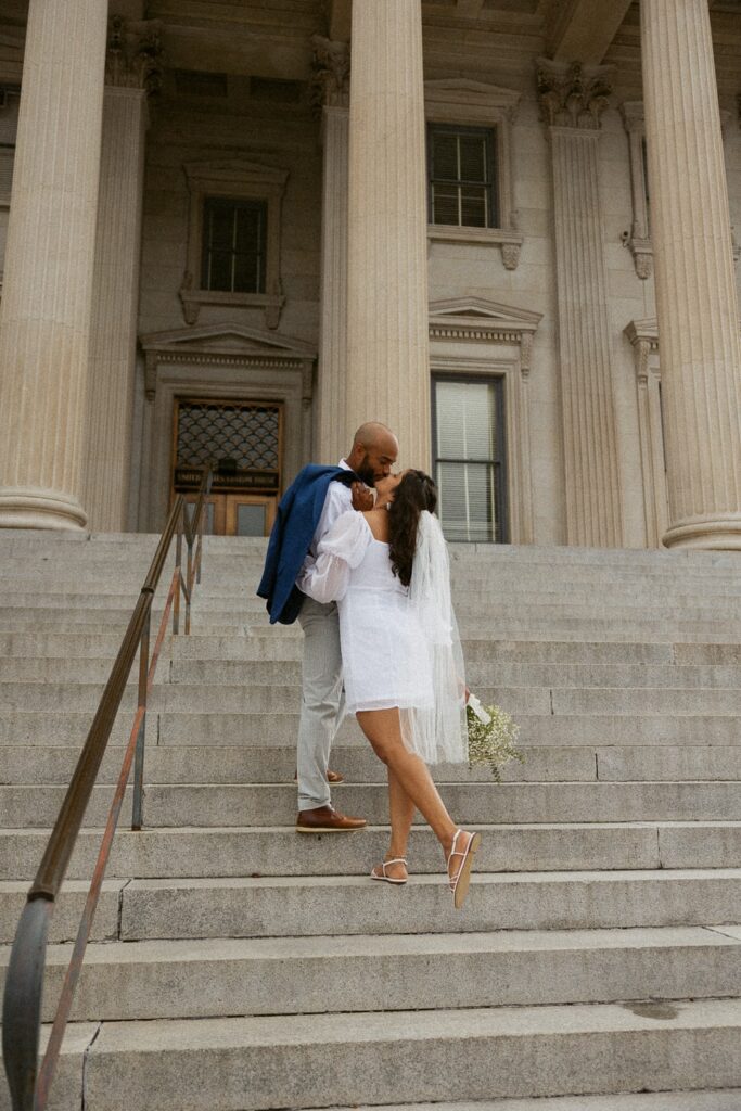 Man and woman standing on courthouse steps and kissing during Charleston wedding.