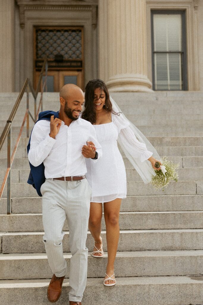 Man and woman running down courthouse steps in wedding attire.