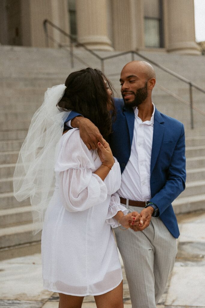 Man and woman hugging and walking in wedding attire at courthouse in Charleston. 