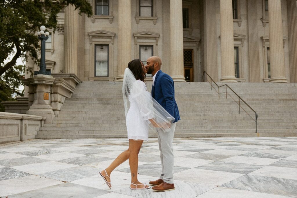 Man and woman in wedding attire kissing in front of courthouse in Charleston.
