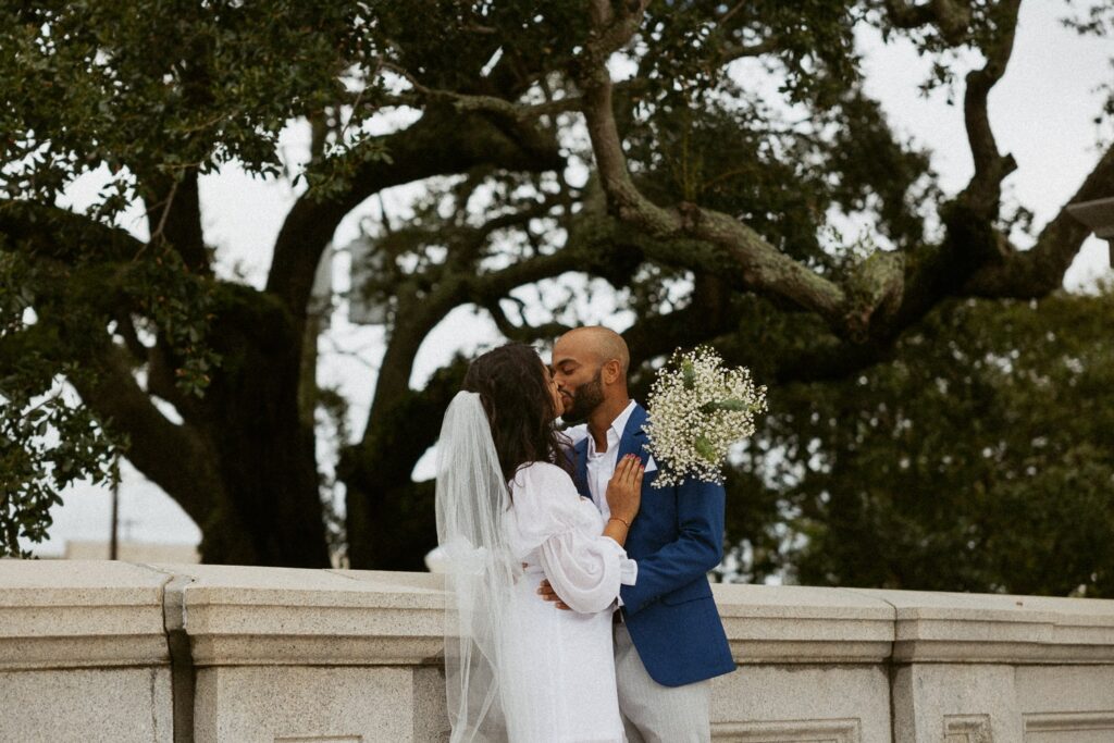 Man and woman kissing underneath a tree and dressed in wedding attire.