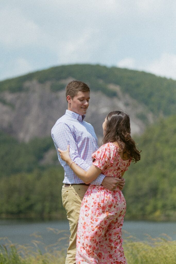 Man and woman smiling at each other and hugging in front of mountain.