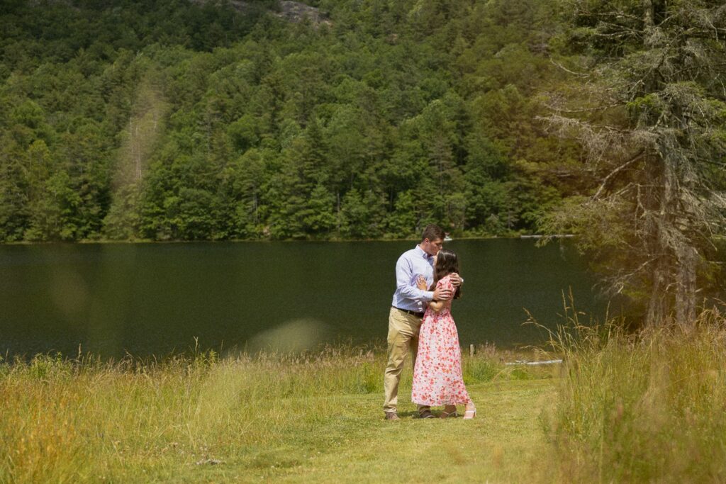 Man kissing woman on the forehead in a field in front of a lake.