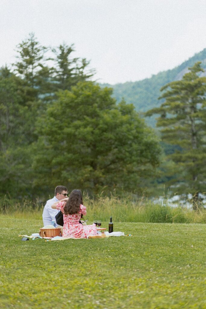 Man and woman sitting on blanket in field having a picnic.