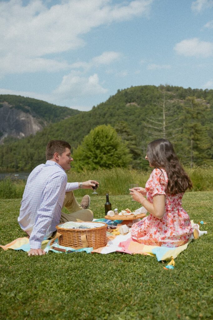 Man and woman smiling at each other while sitting on a blanket having a picnic.