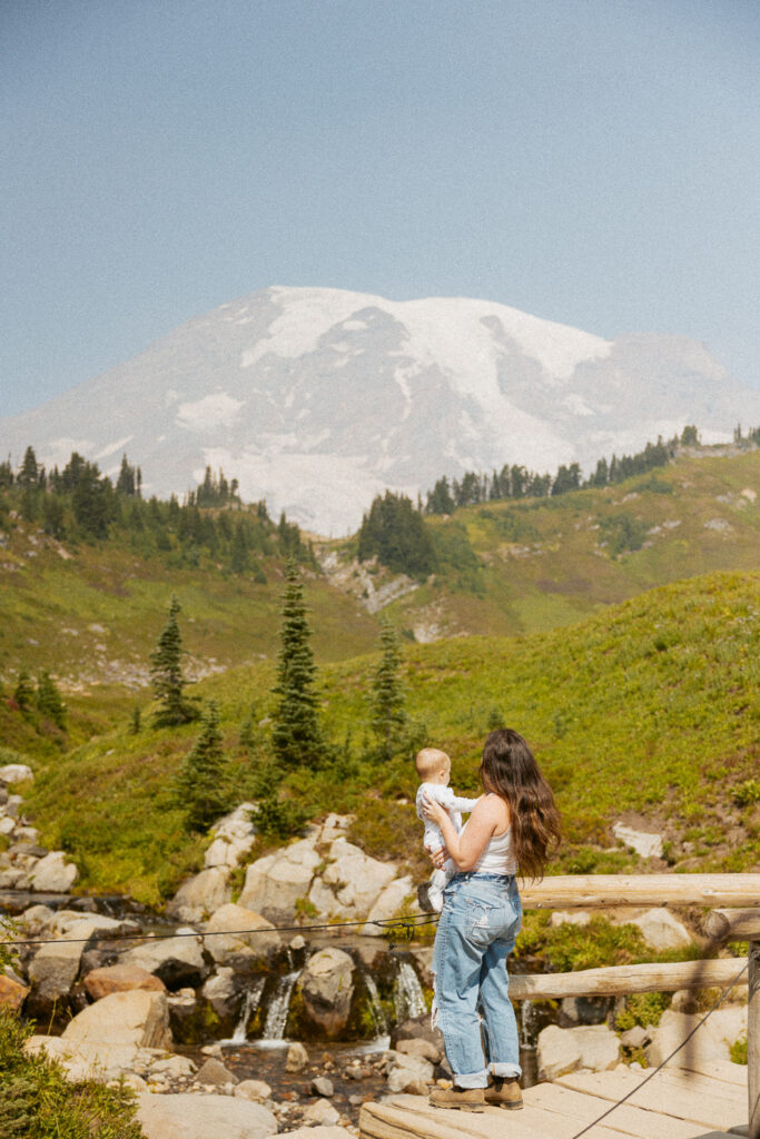 woman holding baby in front of mt rainier.