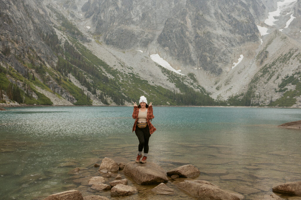 Woman standing on rock in front of alpine lake.