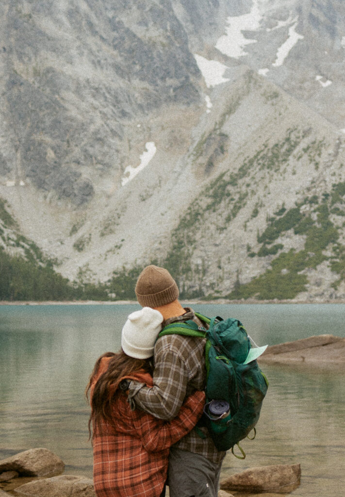 man and woman hugging while looking at alpine lake.