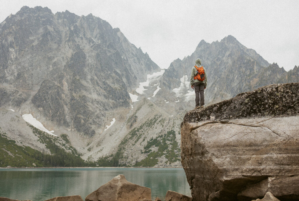 Boy standing on large rock looking out over Colchuck Lake in washington.