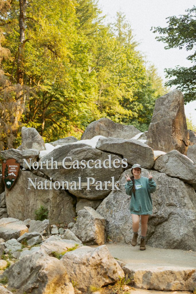 woman holding up peace signs in front of north cascades national park entrance sign.