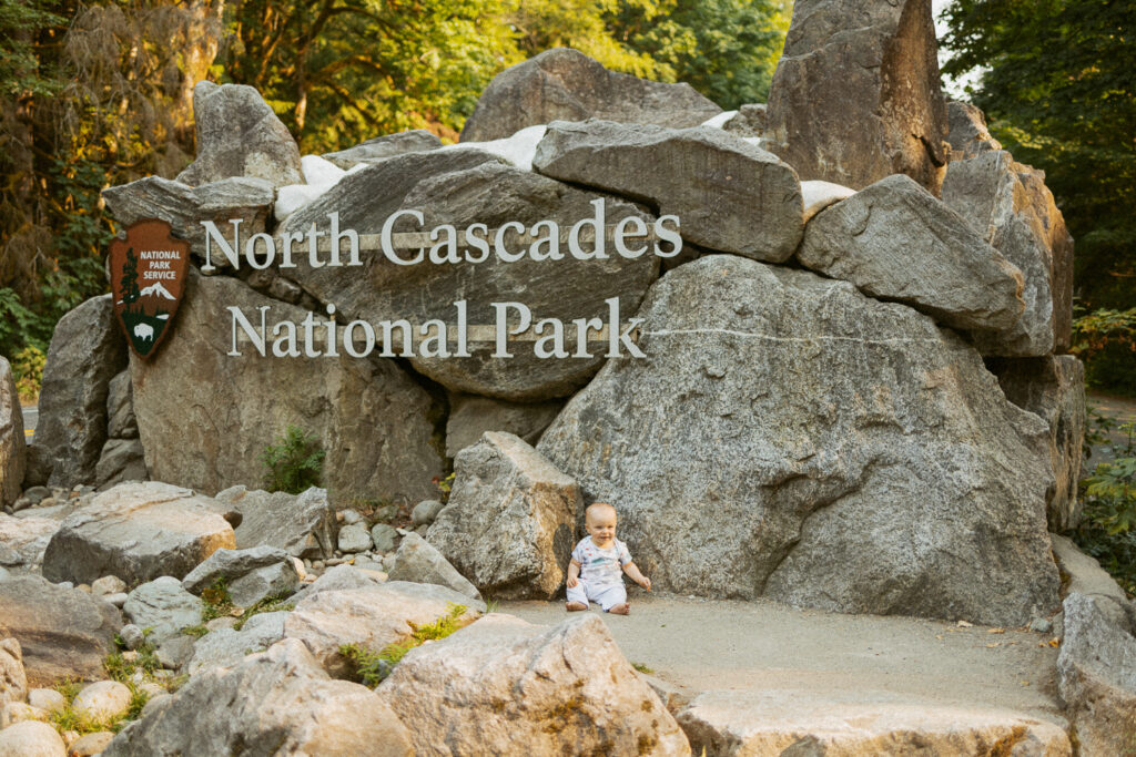 Baby sitting in front of north cascades national park entrance sign.