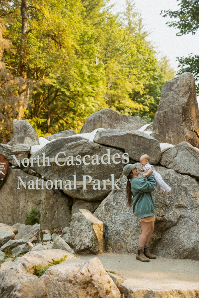 woman holding baby in the air in front of the north cascades national park entrance sign.