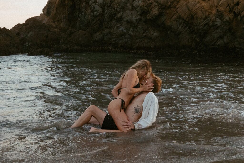 Woman straddling man in the ocean during photoshoot.