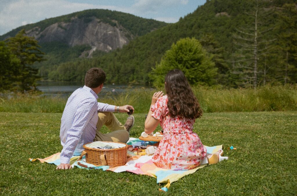 Man and woman sitting on a blanket having a picnic while looking at the mountains.