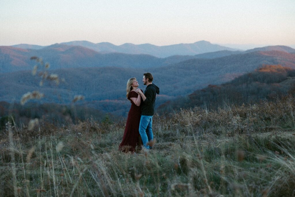 Man and woman dancing and smiling at each other with the mountains in the background.